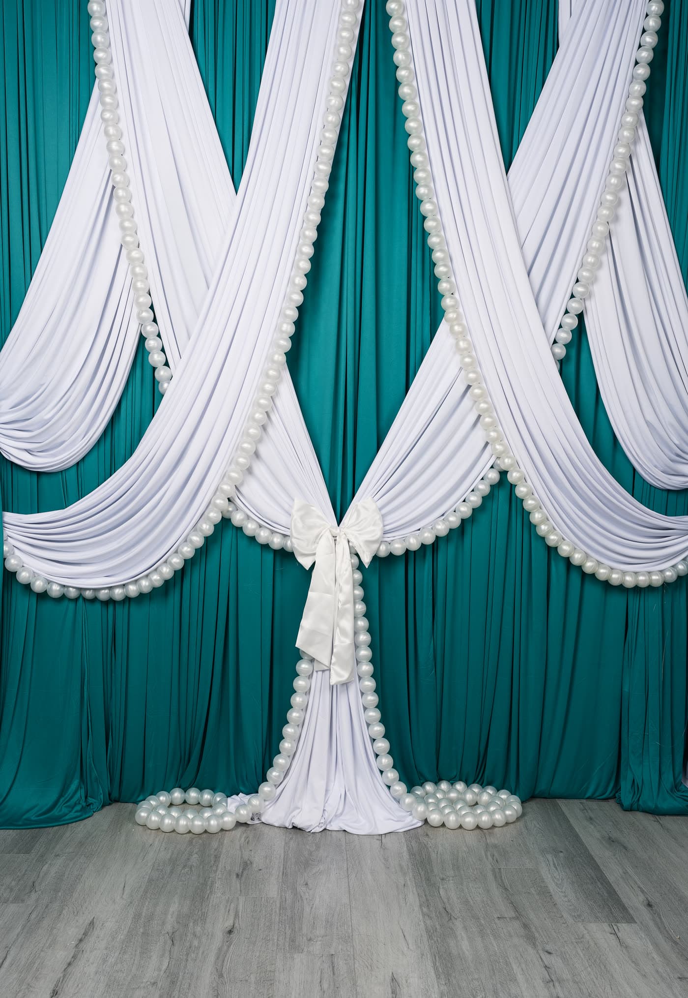 The pearl swag wall on its own: crossed white swags over teal, pearl trim, tied bow