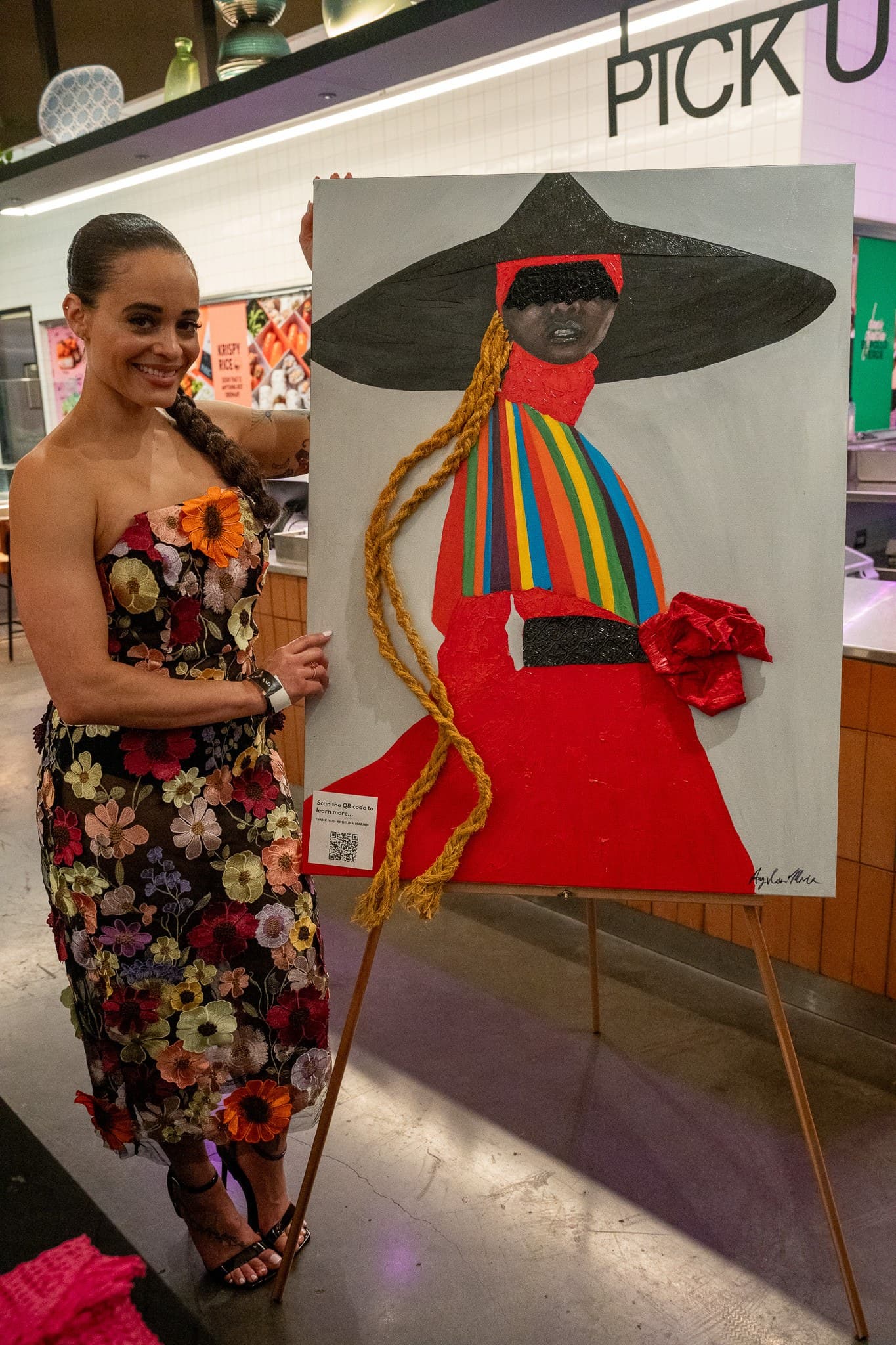Featured artist smiling beside a painting displayed on an easel