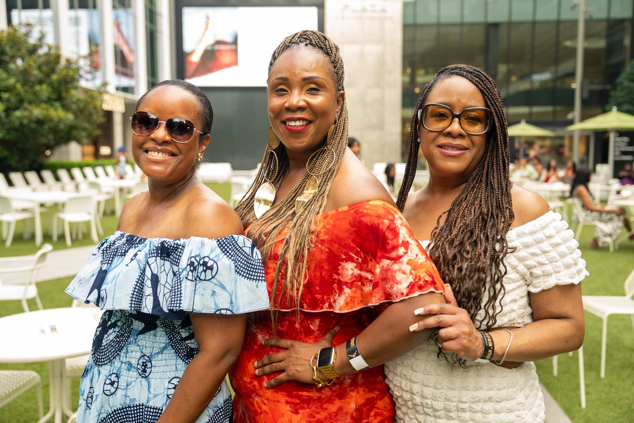 Three guests smiling arm in arm on a lawn at an outdoor daytime event