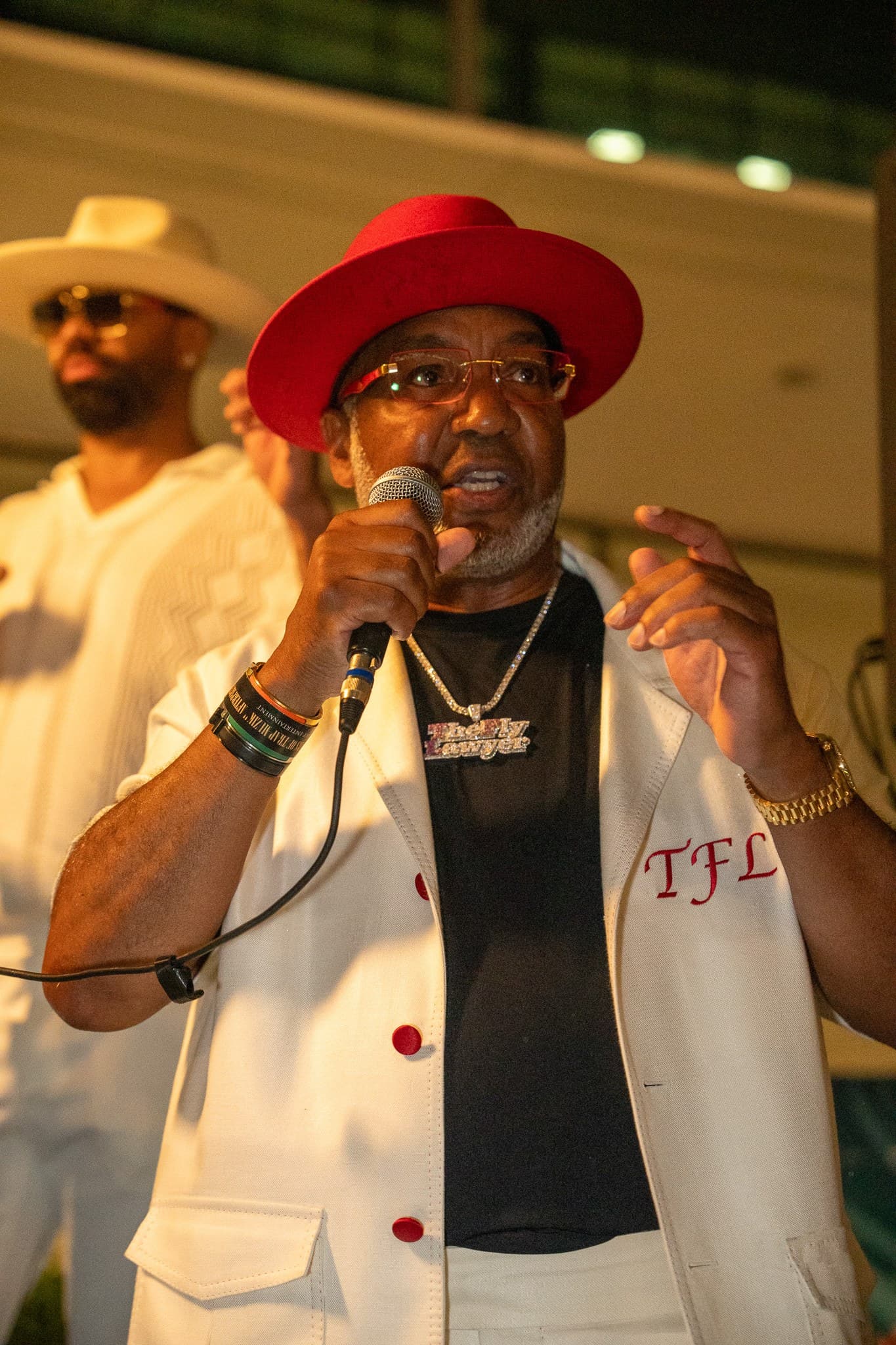 Speaker in a red hat addressing guests with a microphone at an evening event