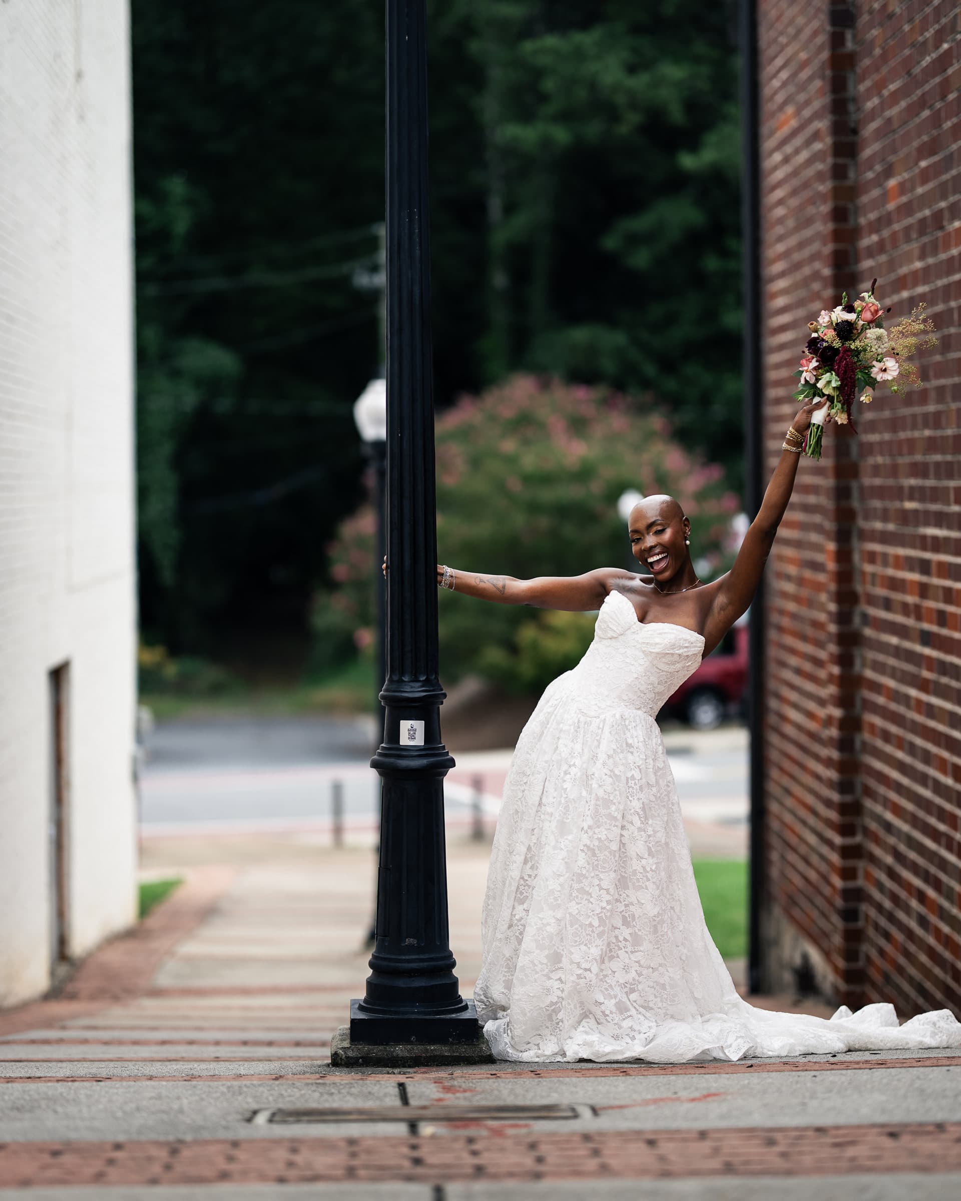 Bride at the lamppost, arms out, brick and trees