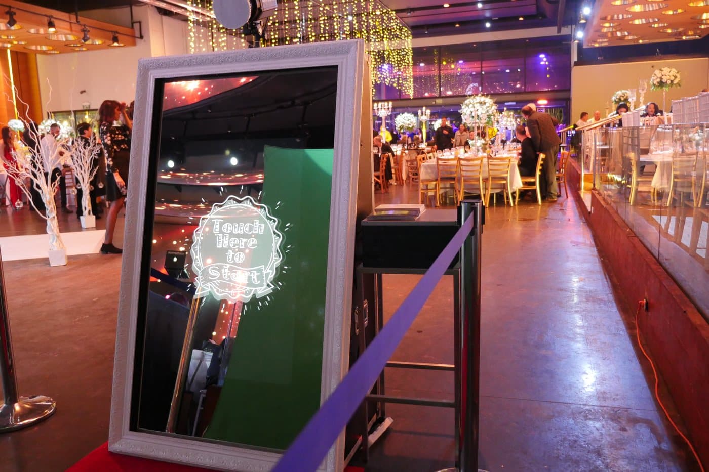 The mirror booth set up in a wedding hall under chandeliers and string lights